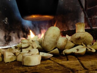 Mushrooms on the wooden kitchen board in front of fireplace and fire flame background