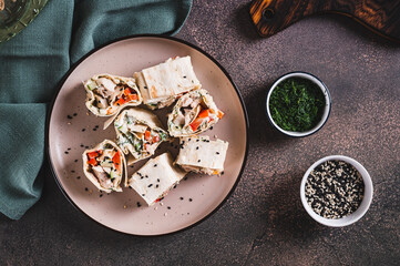 Chicken meat, pepper and cucumber in sauce wrapped in tortilla rolls on a plate top view