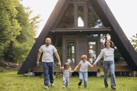 Fototapeta Happy family walking on grass in front of modern a frame house