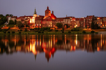 Miasto nad rzeką, krajobraz miejski wieczorową porą, iluminacje świetlne.