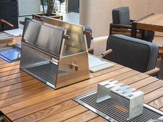 Modern outdoor dining table with built-in stainless steel grills and skewer holders, designed for...