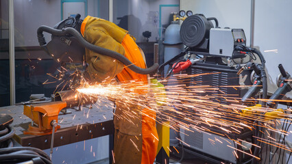 Welder in protective gear grinding metal with bright sparks in a workshop equipped with industrial tools and extraction system. – Metalworking, Manufacturing