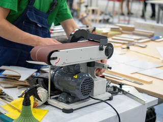 Worker using a belt sander in a woodworking shop to smooth edges and surfaces of wood pieces during furniture or prototype manufacturing. – Woodworking, Manufacturing