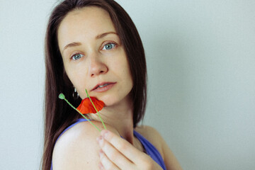 A beautiful brunette young white woman gazes at the viewer, with a red poppy gently resting in her...