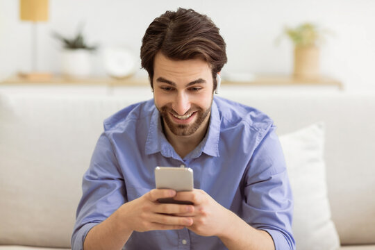 Fototapeta Happy Guy Making Video Call On Cellphone Weaing Earbuds Earphones Sitting On Couch At Home. Modern Distant Communication. Technology And Gadgets, Mobile Application Concept