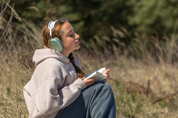 Teenage girl reading a book outdoors. Reading a book and listening to music.