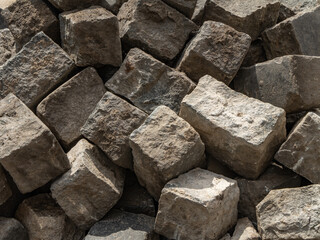 Natural stone paving blocks stacked for road or sidewalk construction. Rough texture, geometric shapes, and earthy tones. Building material background