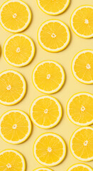 Fototapeta premium Bright yellow lemon slices in pattern on soft pastel yellow background.