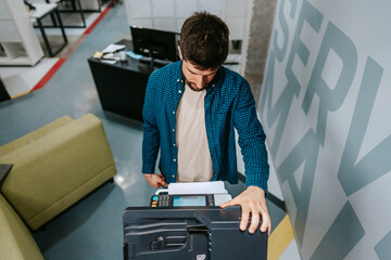 Young man using a copier in a modern office space during the day