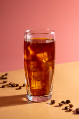Ice coffee with coffee beans in a tall glass on pink background.