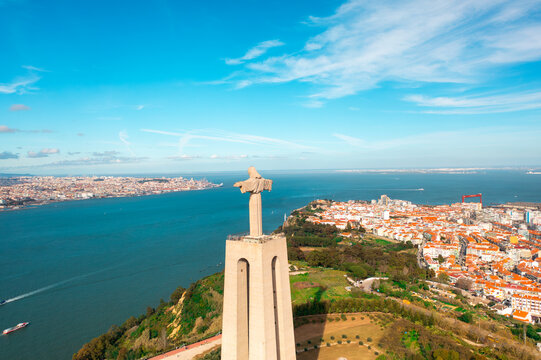 Aerial drone view of monument Sanctuary of Christ the King. Majestic statue overlooks cityscape of Almada and Tagus River under sky