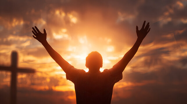 A person's silhouette with arms raised in worship and praise before a cross during a glorious sunset.