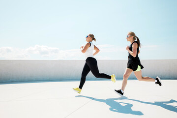 Two women enjoying a vibrant run under the bright blue sky at a rooftop location during the...