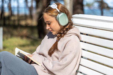 Teenage girl reading a book in the park sitting on a bench. Girl reading a book in the park.