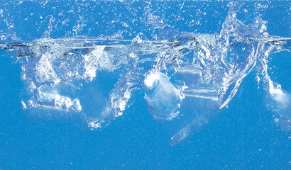 Falling ice tube in motion with splashing water, creating air bubbles scatter around, blue background isolated. Ice tube fall into water with air bubbles