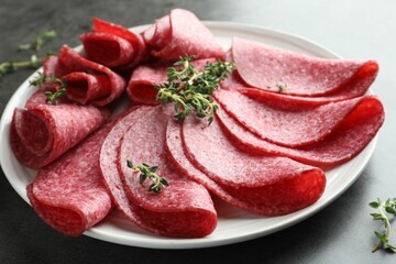 Slices of delicious sausage with thyme served on grey table, closeup