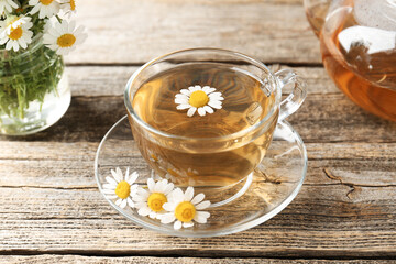 Delicious chamomile tea in glass cup and fresh flowers on wooden table, closeup