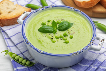 Tasty pea cream soup with basil served on white wooden table, closeup