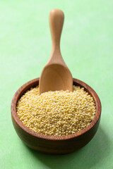 Yellow millet grain in wooden bowl with scoop on green background, Food ingredient
