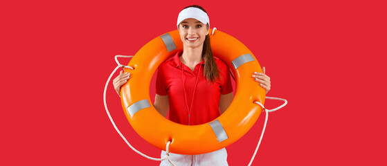 Young pretty female lifeguard in cap with rescue ring on red background