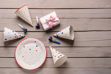Composition with party hats, plate, whistles and gift box on light wooden background