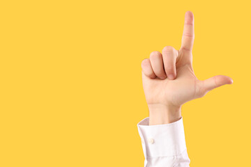 Young businessman showing loser gesture on yellow background