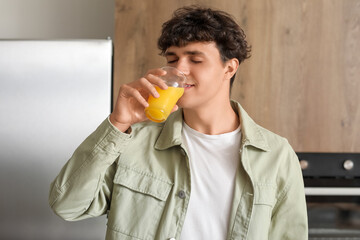 Fototapeta premium Young man drinking orange juice in kitchen, closeup
