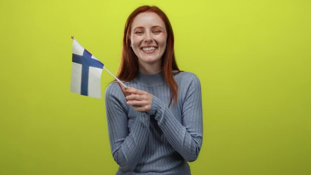 Woman holding finnish flag cheerfully against vibrant yellow background, embodying national pride and joyful expression.