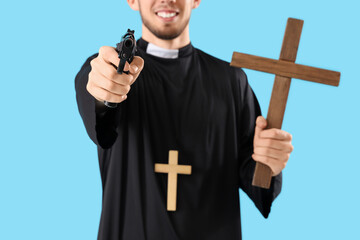 Young priest with gun and cross on blue background, closeup