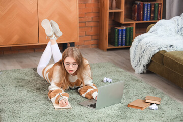 Female author with laptop writing in notebook at home