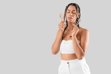 Young African-American woman with dreadlocks and makeup brushes on light background