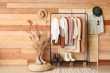 Rack with different stylish clothes and boots in living room