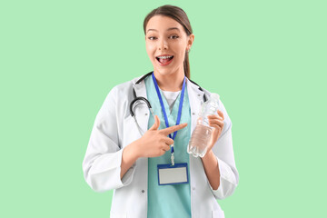 Female doctor pointing at bottle of water on green background