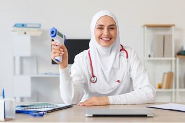 Female Muslim doctor in hijab with infrared thermometer at hospital