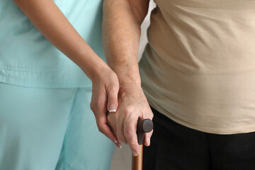 Young nurse and senior woman with walking stick in hospital room, closeup