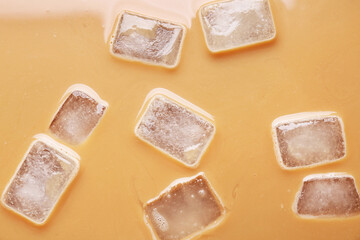 Texture of coffee with milk and ice cubes as background, top view