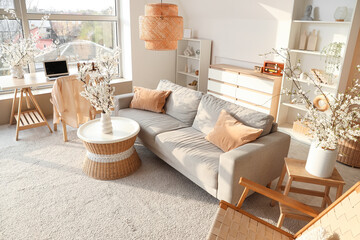 Interior of light living room with sofa and blossoming branches in vases