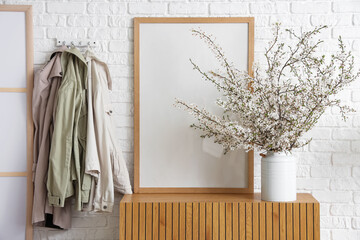 Vase of beautiful blooming branches on commode and hanging clothes in living room