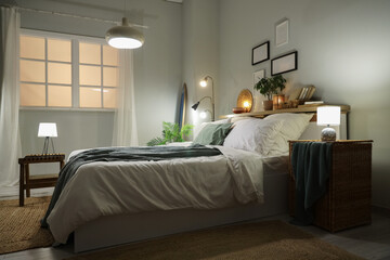 Interior of stylish bedroom with bed, surfboard, glowing lamps and home decor on shelf at evening