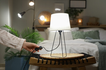 Female hand turning off glowing lamp on wicker table in bedroom at night, closeup
