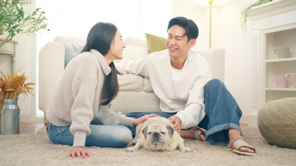 Happy Asian family couple enjoy and fun playing with senior Pug dog breed in living room. Husband and wife relaxing with domestic dog at home. Pet humanization, pet parent and senior pet healthcare. - Powered by Adobe