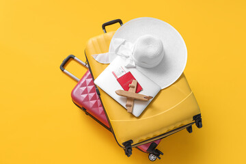 Suitcases with laptop, passport and wooden airplane on yellow background