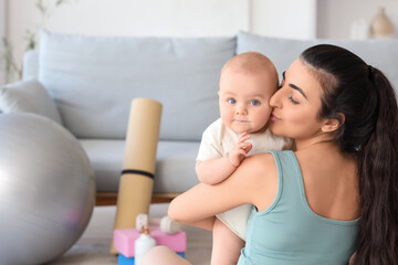 Sporty young woman kissing her little baby at home, back view