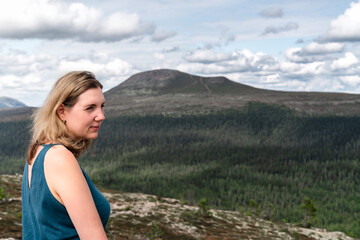 A woman stands on a mountain top, gazing away with the beautiful Städjan mountain visible in the background. In the serene landscape of Idre Dalarna Sweden