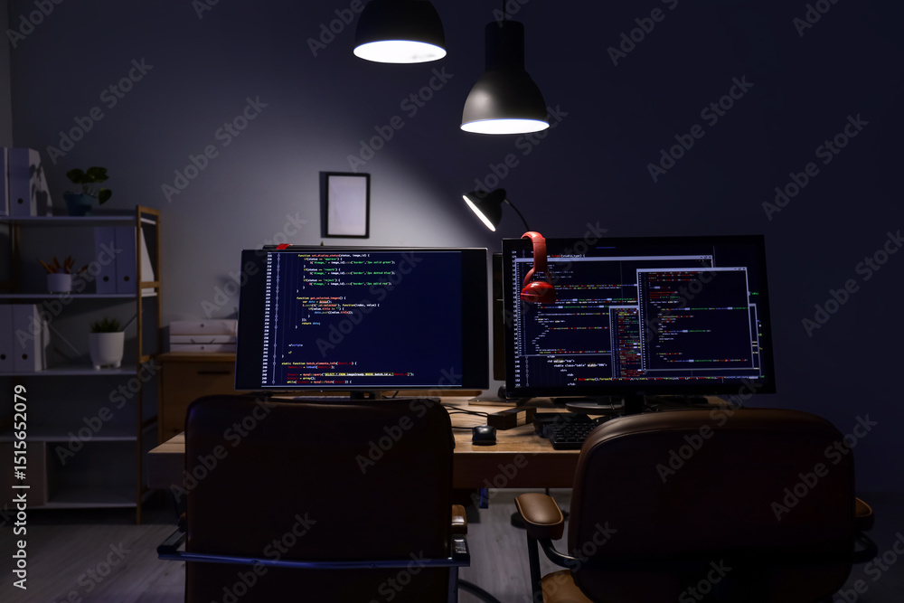 Poster programmer's desk with computer monitors and glowing lamps in dark office at night