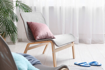 Grey armchair with houseplant, cushion and flip-flops in stylish living room