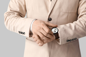 Handsome businessman in stylish beige suit with wristwatch on light background, closeup