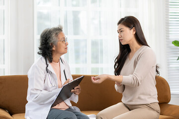 Asian female doctor in white coat attentively listens to young woman during consultation in bright,...
