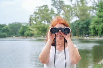 Portrait of a senior Hispanic woman using binoculars smiling and looking at camera. Concept: The...