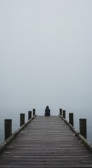 Fototapeta premium Solitude on a Misty Lake: A Person Contemplates on a Wooden Dock in a Foggy Atmosphere